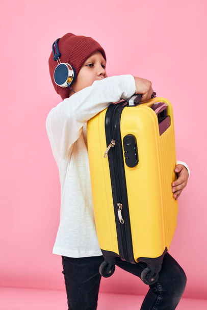 портрет мальчика с желтым чемоданом в руках розовый фон - Фото, изображение