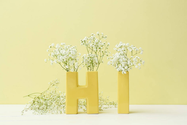 Слово HI і красиві квіти гіпсофіли на столі біля кольорової стіни
 - Фото, зображення