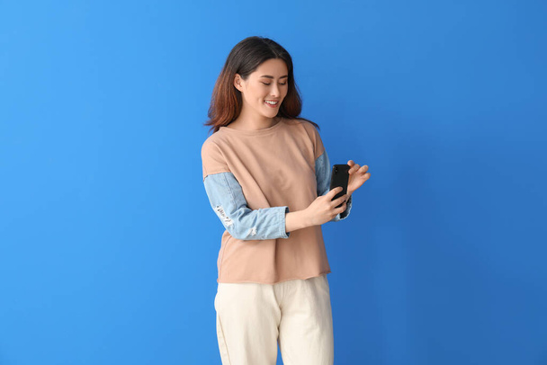 Молодая азиатка с мобильным телефоном на фоне цвета - Фото, изображение