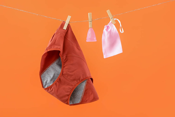 Period panties, menstrual cup and bag hanging on rope against color background - Fotó, kép