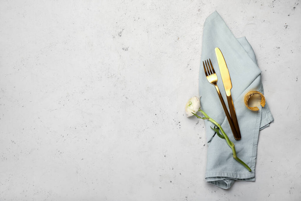 Cutlery, napkin and ranunculus flower on light background - Photo, Image
