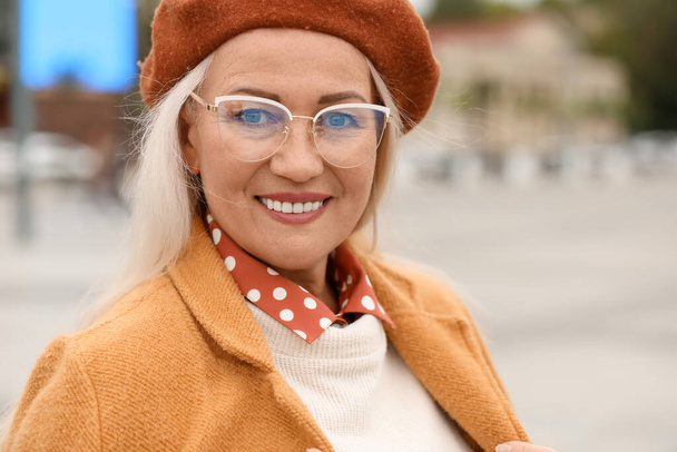Portrait of elegant mature woman wearing stylish eyeglasses and beret hat on city street - Photo, Image
