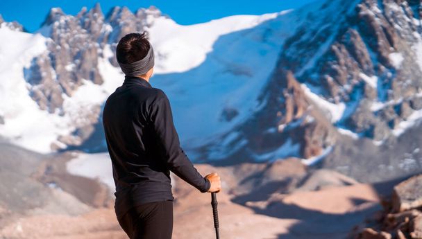 Путешественник с треккинговыми палками идет по заснеженным горам. - Фото, изображение