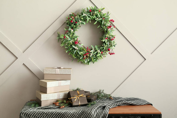 Stůl s dárkovými krabicemi, jedlovou větví a vánočním věncem zavěšeným na lehké stěně, detailní záběr - Fotografie, Obrázek