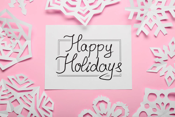 flocos de neve de papel e cartão de saudação com texto HOLIDAYS HAPPY no fundo de cor - Foto, Imagem