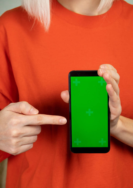Kobieta w czerwonych ubraniach trzyma smartfona z zielonym ekranem w rękach i wskazuje na niego - Zdjęcie, obraz