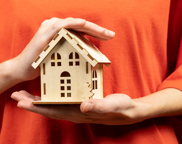 Женщина держит в руках миниатюрный деревянный дом. Концепция покупки, продажи, аренды, страхования недвижимости, ипотеки - Фото, изображение