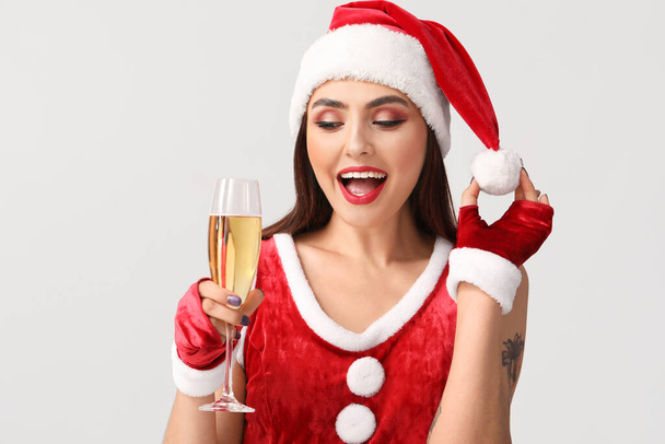 Sexy young woman in Santa costume and with champagne on light background - Φωτογραφία, εικόνα