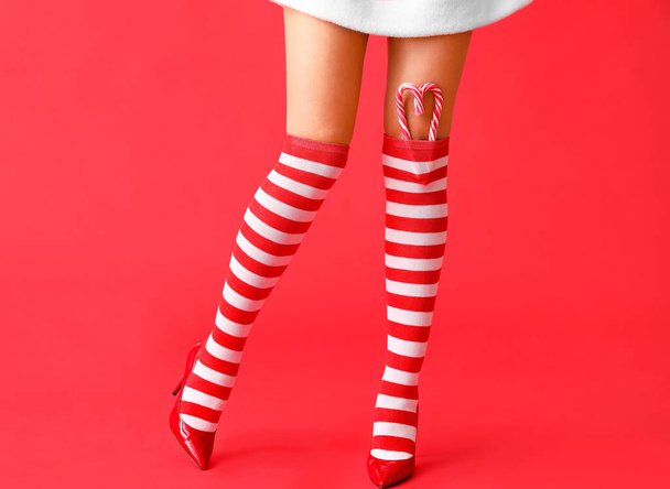 Sexy giovane donna in calze di Natale e con bastoncini di zucchero su sfondo di colore - Foto, immagini