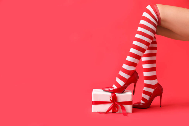 Sexy jonge vrouw in kerstkousen en met cadeau op kleur achtergrond - Foto, afbeelding