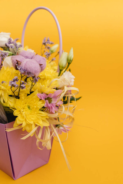 Yellow-violet flower arrangement in a box of chrysanthemums, eustomas, cotton inflorescences and dried flowers on a yellow background - Fotografie, Obrázek