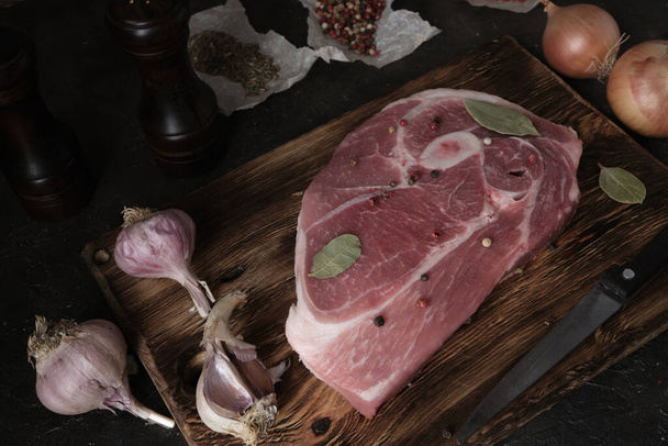 Стейк из сырой свинины на старой разделочной доске, нож, специи и ингредиенты выкладываются бок о бок - Фото, изображение