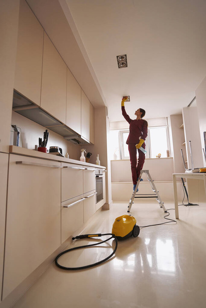 Janitor wiping recessed ceiling luminaires with damp cloth - Foto, afbeelding