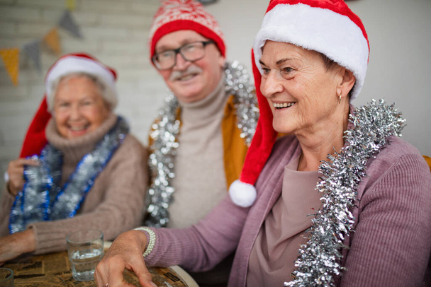 Щасливі старші друзі сидять в приміщенні в громадському центрі і святкують Різдво
. - Фото, зображення
