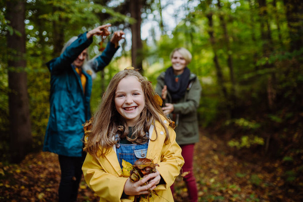 Happy little girl with mother and grandmother having fun with leaves during autumn walk in forest - Foto, Bild
