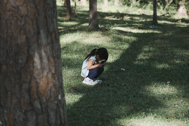 Cute little girl sits on the grass with her eyes closed while playing hide and seek with her family in the park. Happy child spending time with her family on vacation. - Φωτογραφία, εικόνα