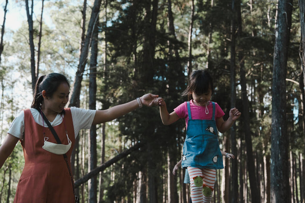 Junge Mutter hilft ihrer Tochter auf einem Baumstamm im Park. Kind auf dem Schwebebalken. Spielen ist Lernen in der Kindheit. - Foto, Bild