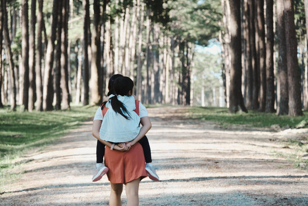 Мила молода донька їде зі своєю матір'ю в парку. Мати тримає дівчину на спині і прогулюється в літньому саду
. - Фото, зображення