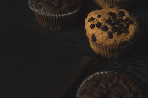 Eine Nahaufnahme von leckeren Schokoladen- und Vanillemuffins mit Schokoladenchips auf schwarzem Hintergrund - Foto, Bild