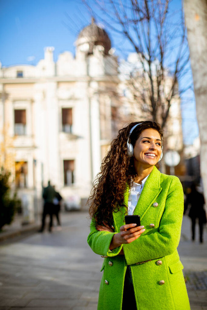 Pretty young woman listening music with smartphone on the street - Zdjęcie, obraz