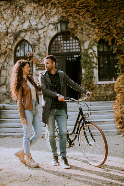 Красивая молодая пара, гуляющая на велосипеде в осеннем парке - Фото, изображение