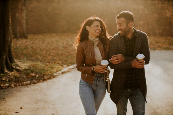 Handsome young couple walking in autumn park with coffee to go cups in hands - Foto, imagen