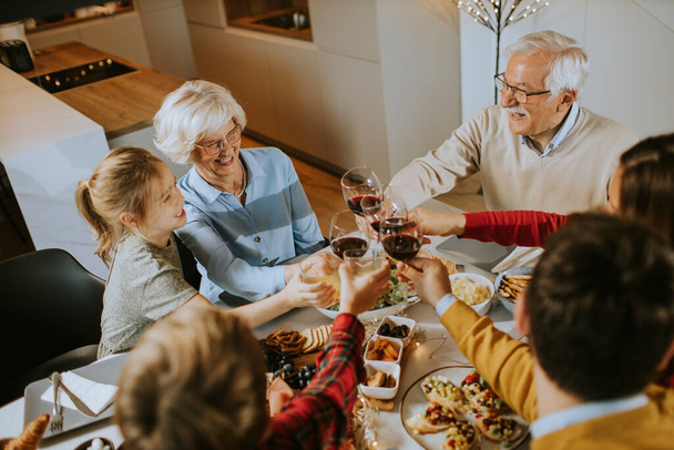 Ευτυχισμένη οικογένεια που τρώει με κόκκινο κρασί στο σπίτι. - Φωτογραφία, εικόνα