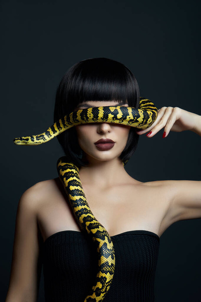 Beauty woman short haircut python yellow snake on her neck. A yellow snake on the shoulders of a girl. Beauty yellow eye shadow makeup, dark burgundy lipstick - Foto, imagen