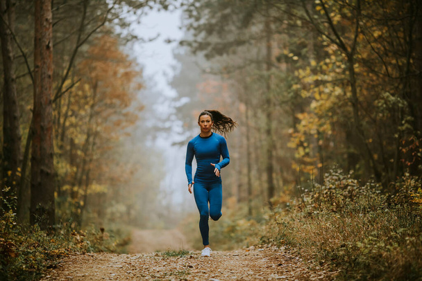 Nuori nainen sinisessä verryttelypuvussa juoksee kohti kameraa metsäpolulla syksyllä - Valokuva, kuva