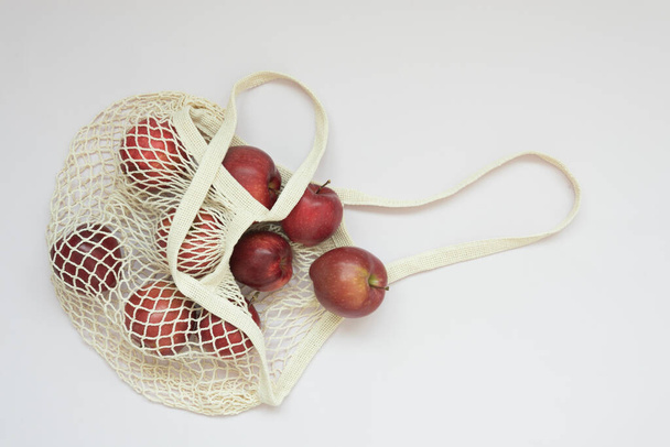 Mesh Shopping Bag. Juicy red apples are in the bag. Delicate pink background. Caring for the Environment. Healthy, organic fruits - 写真・画像