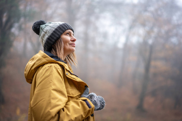 Aantrekkelijke jonge vrouw in geel park en hoed genieten van frisse lucht in de herfst mistige bos - Foto, afbeelding