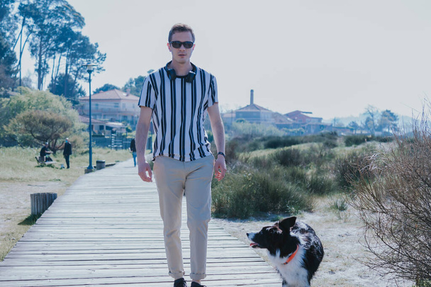 man with headphones walking with his dog on the beach walkway - Valokuva, kuva