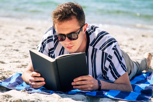 man lying relaxed on his towel on the beach reading a book - Fotó, kép