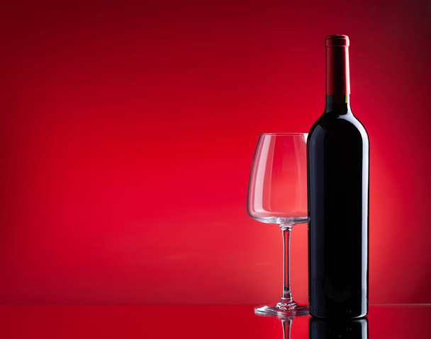 Красный бокал вина и бутылка на красном фоне с копировальным местом - Фото, изображение
