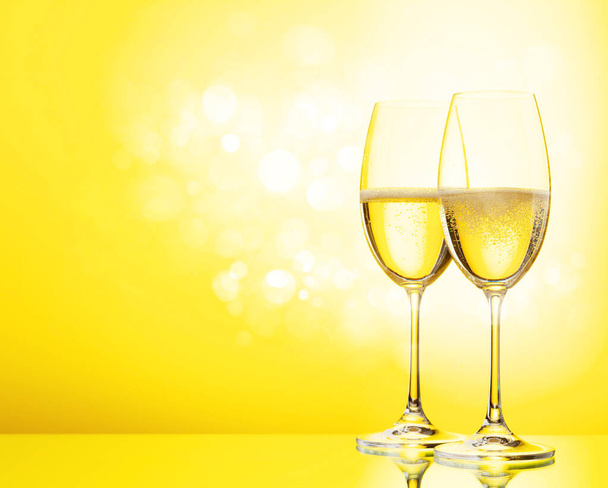Δύο ποτήρια σαμπάνιας και μπουκάλι αφρώδους κρασιού. Πάνω από κίτρινο φόντο - Φωτογραφία, εικόνα