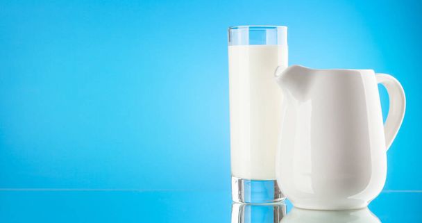 Milk pitcher and glass over blue background with copy space. Dairy product - Фото, зображення