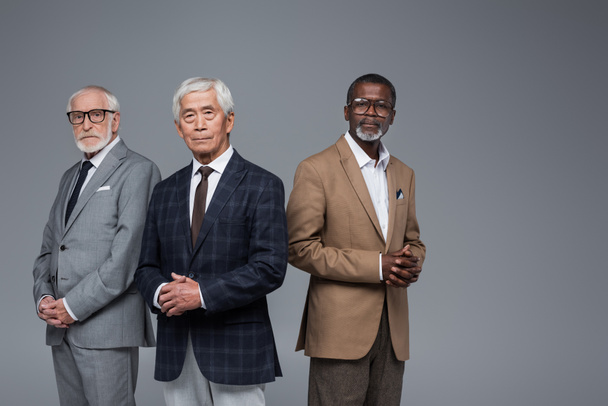 hochrangige und selbstbewusste multiethnische Unternehmensmanager blicken isoliert auf graue Kameras - Foto, Bild