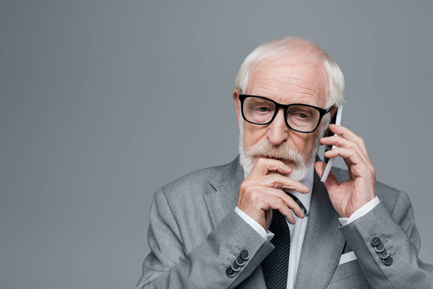 doordachte oudere zakenman in gesprek op mobiele telefoon geïsoleerd op grijs - Foto, afbeelding