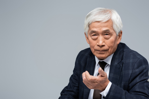 vanhempi aasialainen liikemies ojennetulla kädellä katsoen kameraa eristettynä harmaalla - Valokuva, kuva