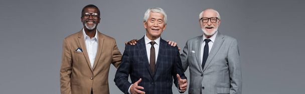 successful senior multiethnic businessmen smiling at camera isolated on grey, banner - Foto, afbeelding