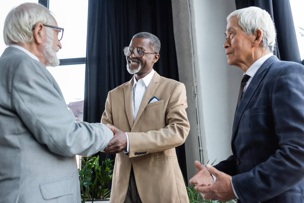 senior asian businessman looking at business partners shaking hands in office - Foto, imagen
