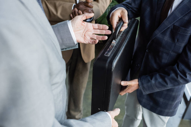 vista recortada del hombre dando maletín a socios comerciales multiétnicos - Foto, Imagen