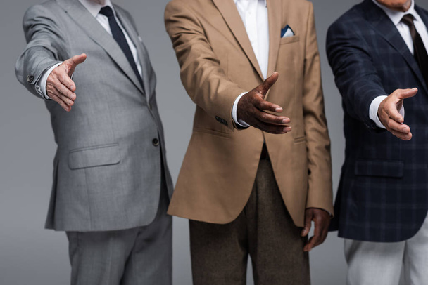 cropped view of senior multiethnic businessmen with outstretched hands isolated on grey - Foto, afbeelding