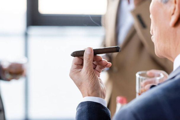 cropped view of senior businessman smoking cigar in office - Foto, afbeelding