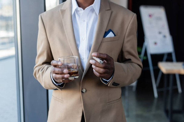 levágott kilátás vezető afro-amerikai üzletember szivarral és pohár whiskyvel az irodában - Fotó, kép
