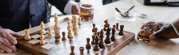 cropped view of business partners with glasses of whiskey playing chess in office, banner - Foto, Imagen