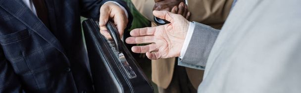 partial view of senior man holding briefcase near interracial business partners, banner - Photo, Image