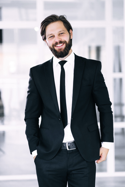 Portrait of a happy smiling young businessman straightening his jacket against the background of windows. Business success concept. - Foto, Imagem