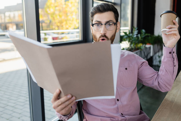 Amazed businessman holding blurred paper folder and coffee to go in office  - Photo, Image