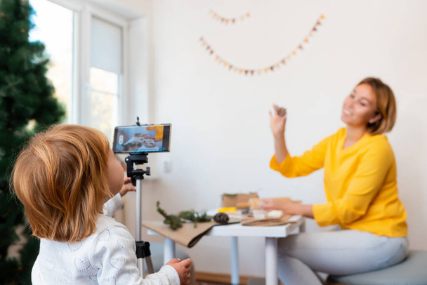 A young mother and her daughter record a video stream together. A little girl helps her mom to record a vlog. The concept of video streaming. - Valokuva, kuva
